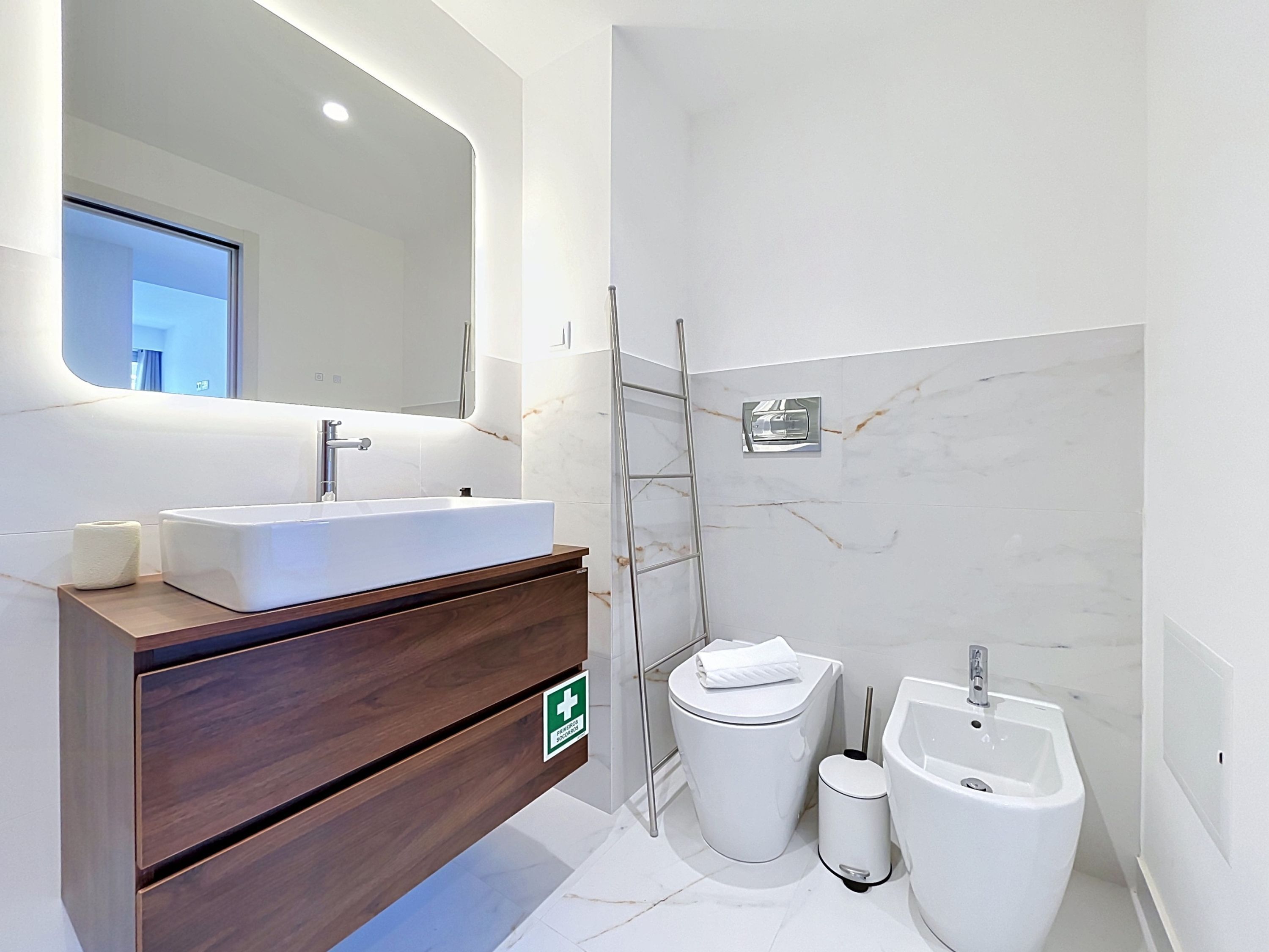 A modern bathroom with a large mirror, a sink, a toilet, and a bidet.
