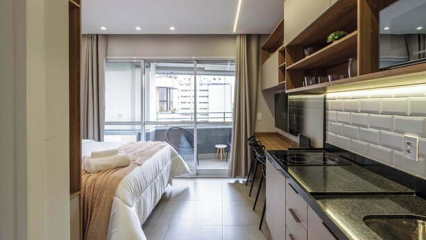 Ein modernes Hotelzimmer mit Bett, Küchenzeile und Balkon mit Blick auf die Stadt.
