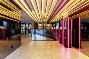 Um hall de hotel moderno com um balcão de recepção de mármore, divisória de vidro e teto com iluminação linear.
