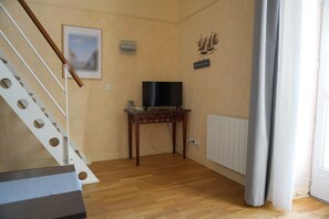 A living room with a wooden floor, a TV on a stand, a staircase with circular cutouts, and a radiator. - 3-person apartment (Le Croisic)