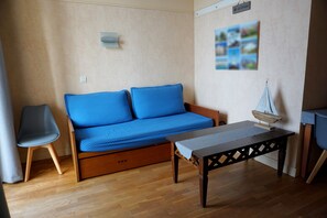 A room with a wooden sofa, a small table, a chair, and a wall-mounted shelf. - 3-person apartment (Le Croisic)