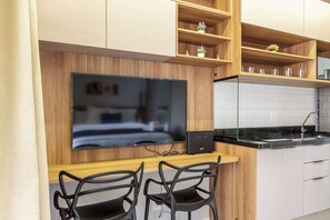 Eine moderne Küche mit Flachbildfernseher, Holzregalen, einer schwarzen Arbeitsplatte und zwei schwarzen Stühlen.