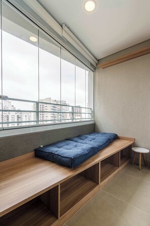 Ein Zimmer mit Fenster, einer Bank, einem kleinen Tisch und Blick auf Gebäude.