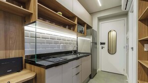 Una cocina moderna con encimera negra, electrodomésticos de acero inoxidable, estantes de madera y una puerta blanca.