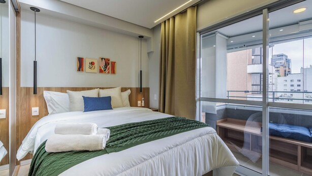 Habitación de hotel con una cama grande, vistas a la ciudad y un balcón con sofá.