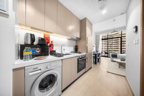 A modern kitchen with a washing machine, a coffee maker, and a fire extinguisher. - Free housekeeping visits during your stay - StayShort - Beauriful Modern Studio that Sleeps 4 at Riviera Beachfront (Meydan)