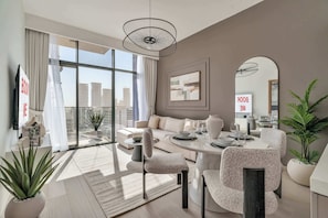 A modern living room with a sofa, dining table, chairs, a TV, and large windows. - Free housekeeping visits during your stay - StayShort - Chic Modern 1BR that Sleeps 4 at Riviera Beachfront (Meydan)