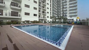 A swimming pool with a tiled edge, surrounded by a brick deck, and adjacent to a multi-story residential building with balconies. - Spacious Studio Apartment that Sleeps 4 (JVC)