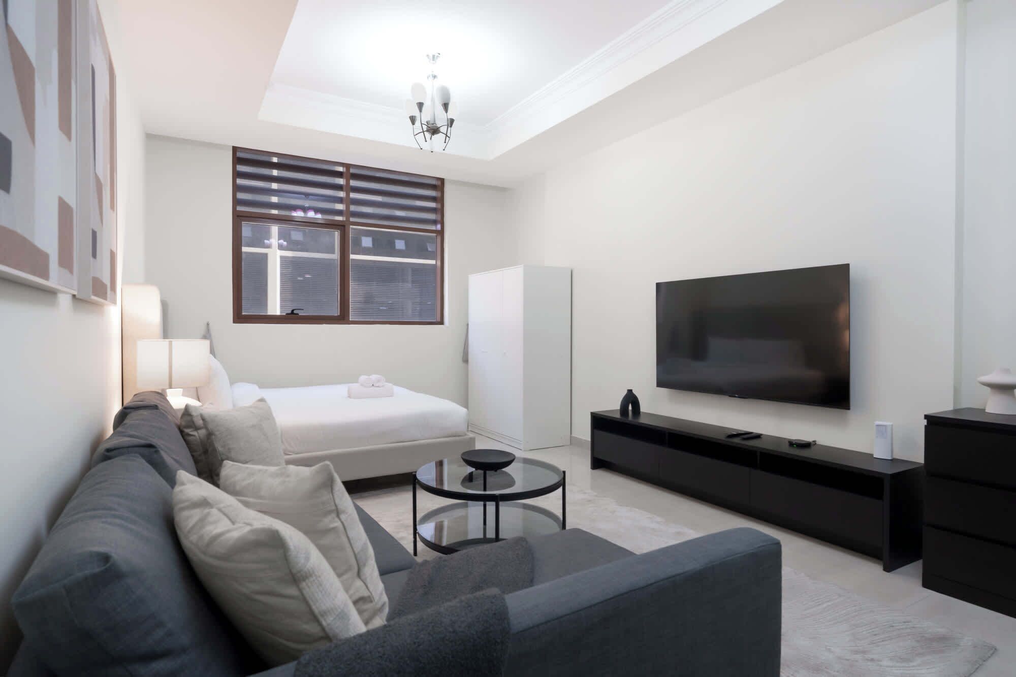 A modern living room with a sofa, a small round table, a TV, and a wardrobe.