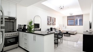 A modern kitchen with a central island, a dining area with a sofa and table, and a living area with a sofa and a TV. - Spacious Studio Apartment that Sleeps 4 (JVC)