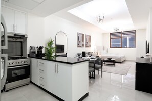Eine moderne Küche mit Kochinsel, ein Essbereich mit Sofa und Tisch sowie ein Wohnbereich mit Sofa und Fernseher.