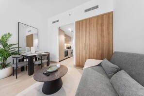 A modern living room with a grey sofa, a dining table with chairs, a coffee table, a large mirror, and a wooden wardrobe. - Free housekeeping visits during your stay - StayShort - Modern Studio that Sleeps 4 at Riviera Beachfront (Meydan)