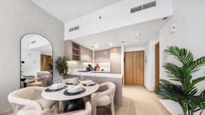 A modern kitchen with built-in appliances, a dining area with round tables and cushioned chairs, and a large mirror. - StayShort - Modern 1BR that Sleeps 4 at Riviera Beachfront (Meydan)