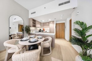 Een moderne keuken met inbouwapparatuur, een eetgedeelte met ronde tafels en stoelen met kussens, en een grote spiegel.