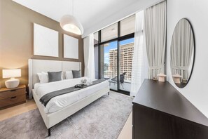 Een moderne slaapkamer met een groot bed, een dressoir, een spiegel en uitzicht op een gebouw.