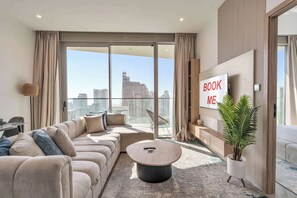 Ein modernes Wohnzimmer mit einer großen Couch, einem Couchtisch und Blick auf die Stadt durch raumhohe Fenster.