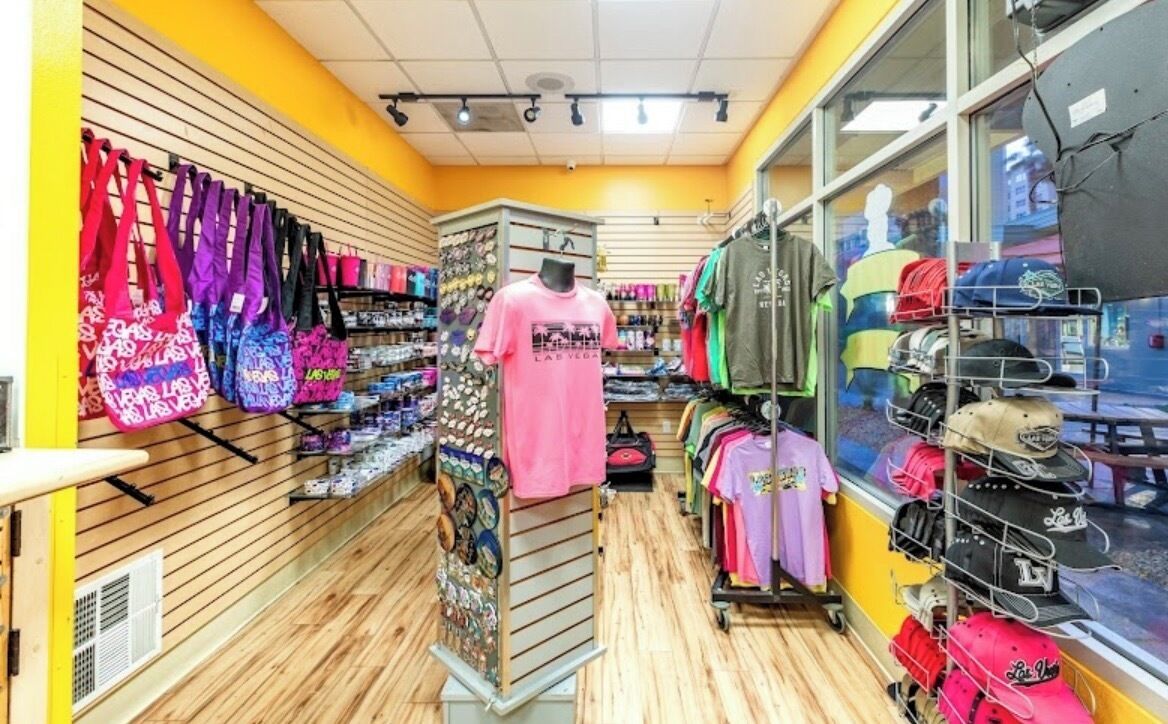 En butik med reoler fyldt med farverige tasker, en mannequin i en lyserød skjorte og hatte på stativer.
