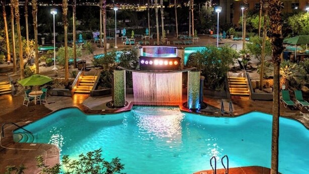 A nighttime swimming pool with a waterfall feature, surrounded by palm trees and lounge chairs. - Spacious 4-bedroom condo in peaceful Las Vegas with AC and gym (Las Vegas)