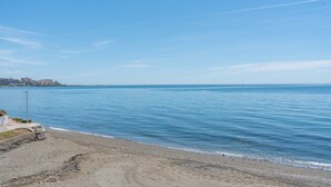 A beach with clear blue water, a sandy shore, and a distant cityscape.