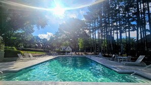 Une piscine à l’eau claire, entourée de chaises longues et de grands arbres.