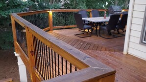 Une terrasse en bois avec une table et des chaises, un barbecue et une fenêtre avec des stores.