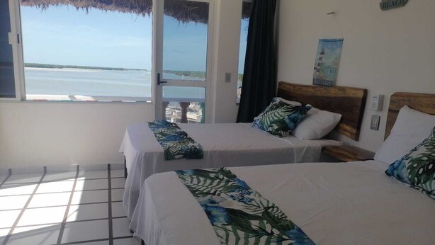 A hotel room with two beds, a view of the sea, a thatched roof outside, and a wooden headboard. - Macumba Hotel and Restaurant The best view of the Ria Lagartos. (Río Lagartos)