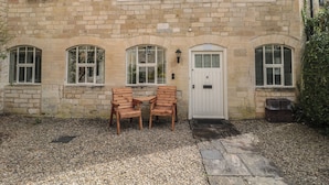 A stone building with a white door, two wooden chairs, and a gravel driveway. - Longfords Mill, Minchinhampton (Stroud)