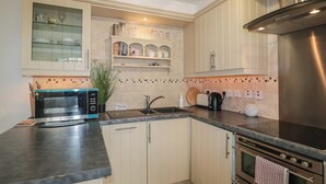 A kitchen with a microwave, toaster, sink, and stainless steel range hood. - Longfords Mill, Minchinhampton (Stroud)