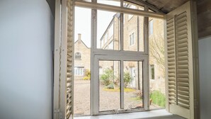 A room with a window overlooking a courtyard, a wooden ceiling, and a white wall. - Longfords Mill, Minchinhampton (Stroud)