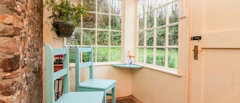 A room with two chairs, a small table, a hanging plant, and a view of greenery through large windows.