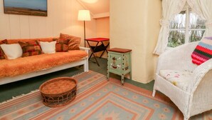 A cozy room with a sofa, a small table, a wicker chair, a window with curtains, and a painting on the wall. - Whitefield Cottage (Barnstaple)