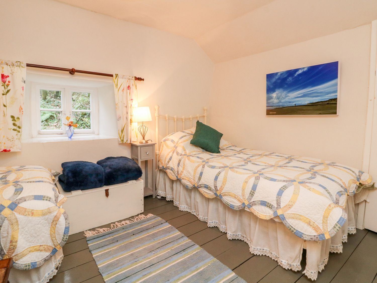 Un dormitorio con cama, ventana con cortinas, mesita de noche con lámpara, un cuadro en la pared y alfombra en el suelo.