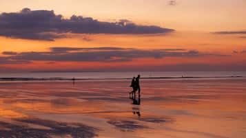 Uma praia ao pôr do sol com uma pessoa caminhando na areia.