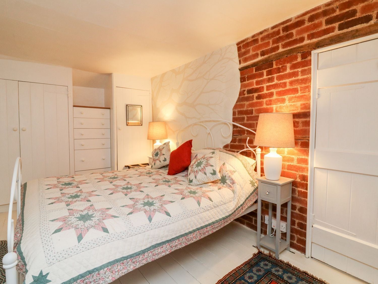 Une chambre à coucher avec un lit, deux lampes de chevet, une table de chevet, une armoire blanche et un mur en briques.