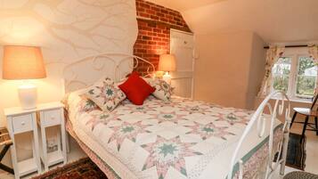 Quarto com cama, duas mesas de cabeceira, travesseiro vermelho, colcha, parede de tijolos, janela e uma cadeira.