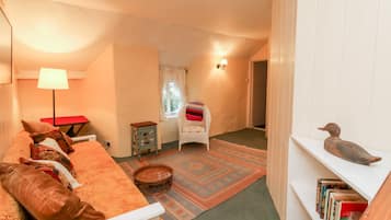 Una habitación acogedora con sofá, una pequeña mesa, lámpara, silla, estantería y ventana.