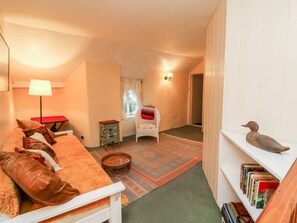 A cozy room with a sofa, a small table, a lamp, a chair, a bookshelf, and a window. - Whitefield Cottage (Barnstaple)