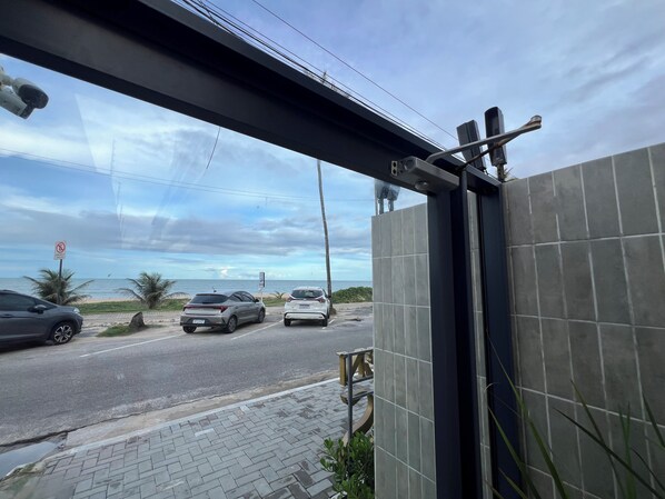 Une vue à travers la fenêtre d’un bâtiment dont le mur est recouvert de carreaux, une rue avec des voitures et un ciel dégagé.