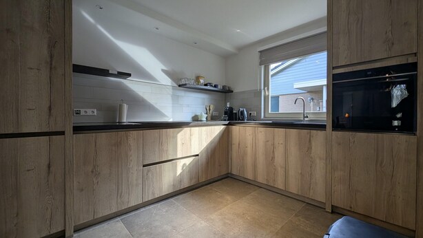 Una cocina moderna con armarios de madera, encimera negra y una ventana que deja entrar luz natural.