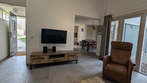 Una sala de estar moderna con un televisor de pantalla plana, mueble de entretenimiento de madera, sillón de cuero y un área de comedor al fondo.
