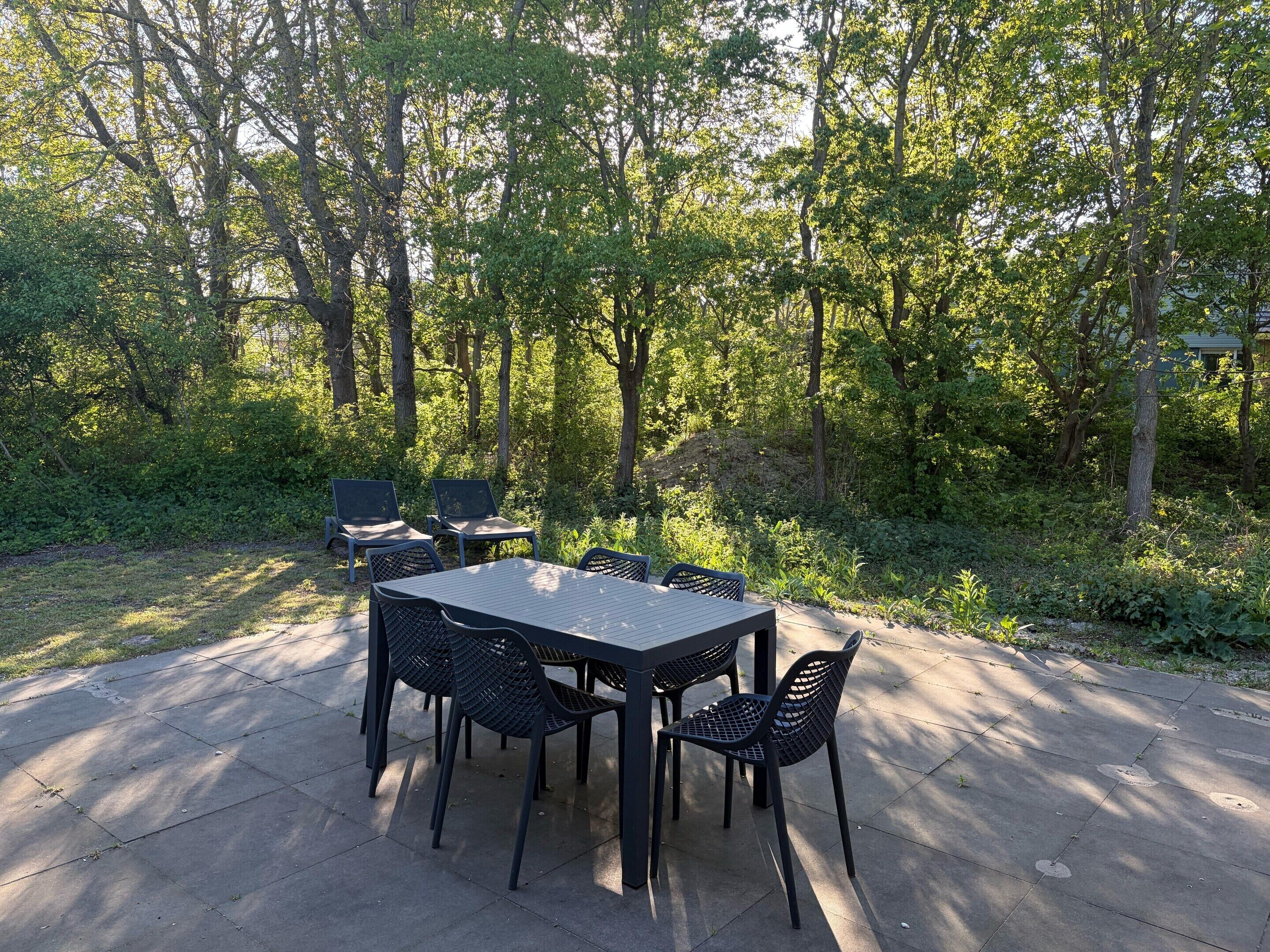 Une terrasse extérieure avec une table et des chaises, entourée d’arbres.