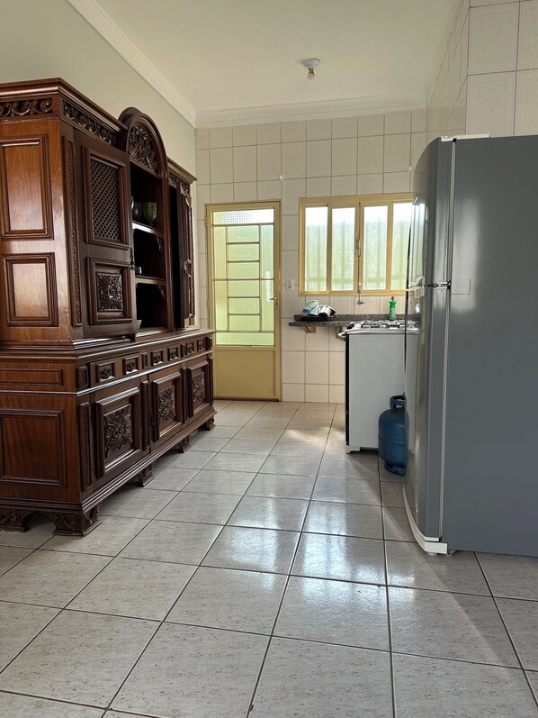 Een keuken met een houten kast, een koelkast, een gasfornuis en een raam.