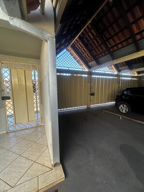 A covered parking area with a car, a gated entrance, and a tiled floor. - Billuca 2 Residential Complex (Várzea Grande)