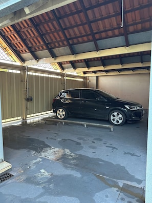 A car parked inside a garage with a metal gate, a concrete floor, and a sloped ceiling. - Billuca 2 Residential Complex (Várzea Grande)