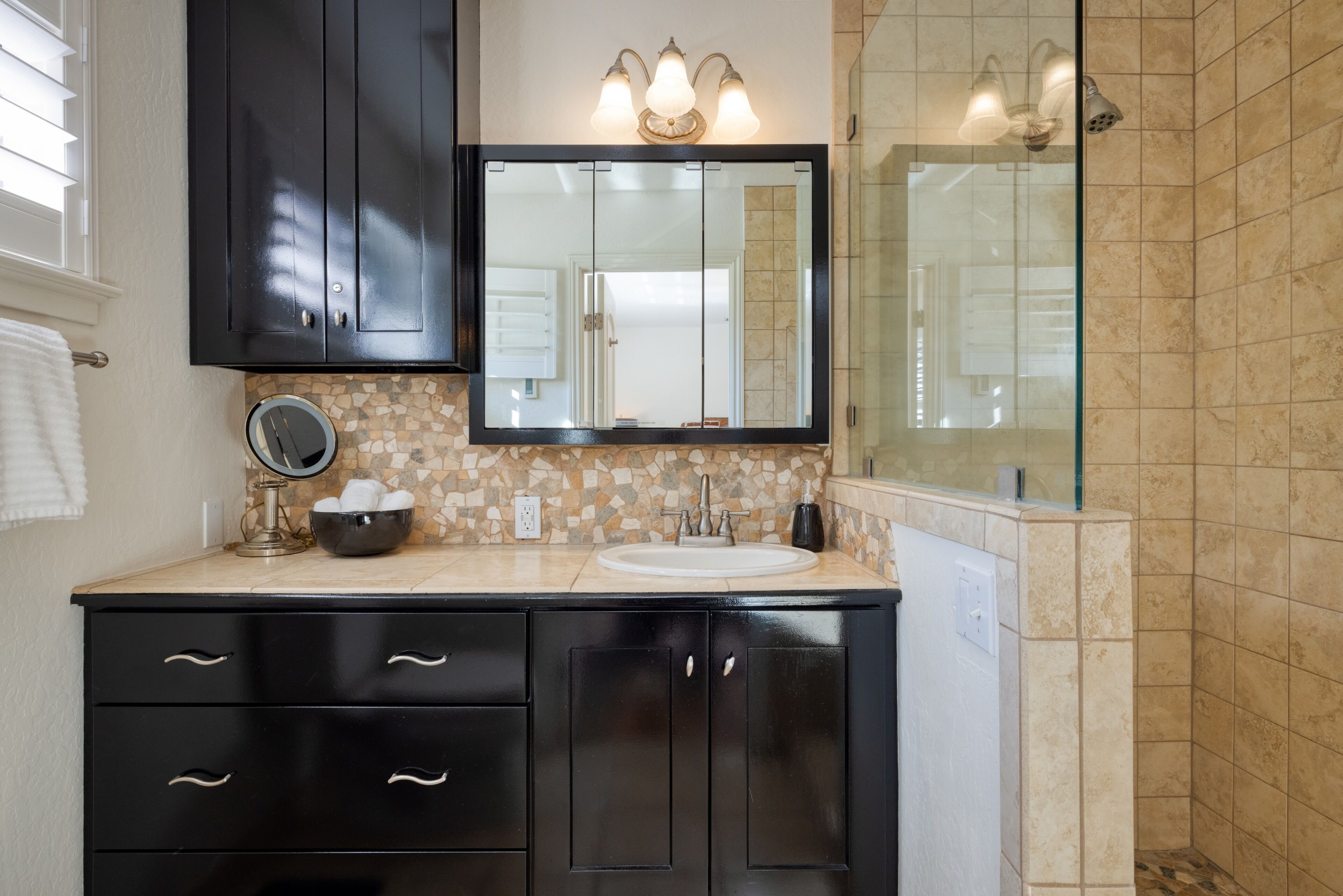 Une salle de bain avec un meuble-lavabo noir, un miroir rond, un lavabo et un espace douche.