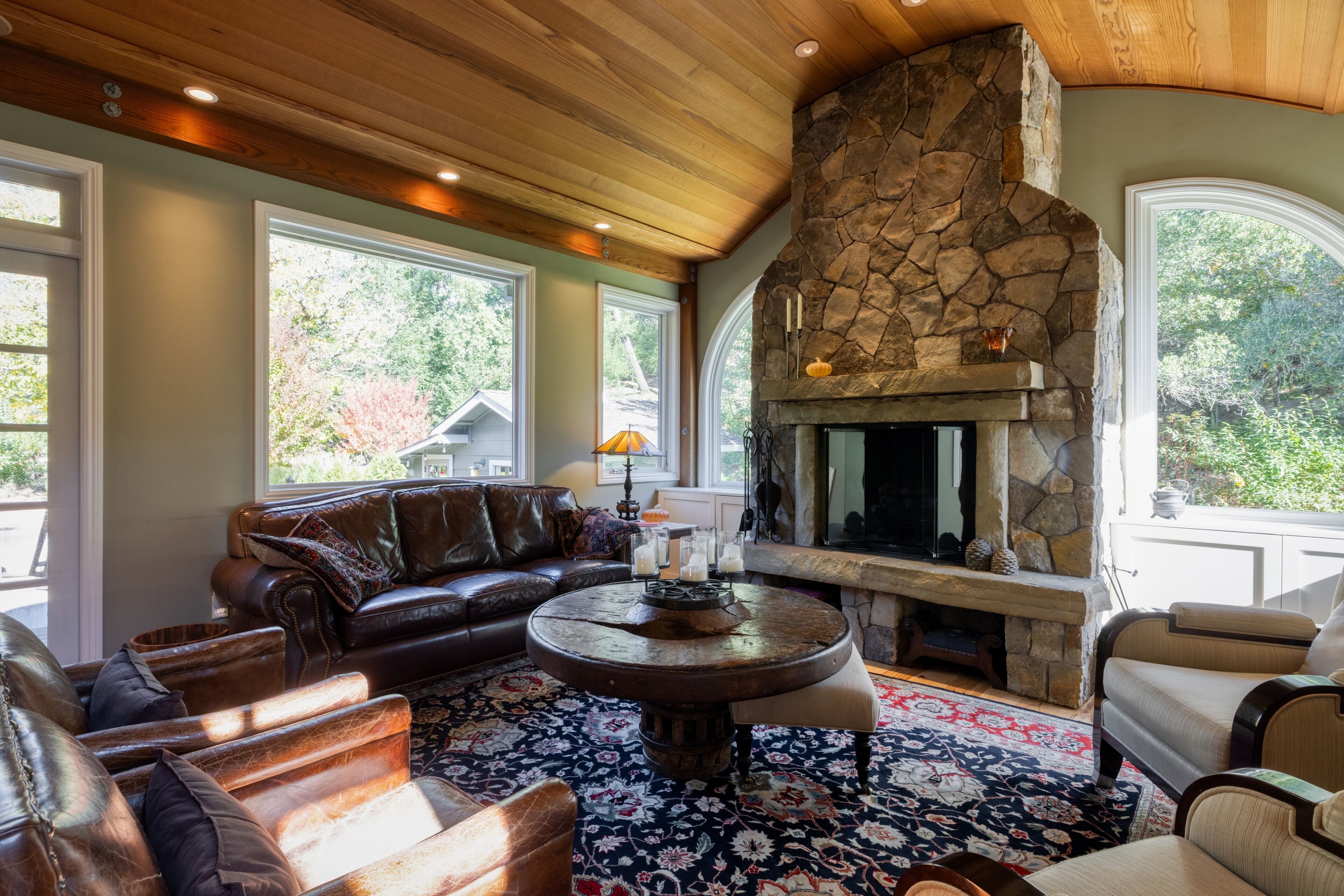 Una sala de estar acogedora con chimenea de piedra, mobiliario de cuero y ventanas amplias.