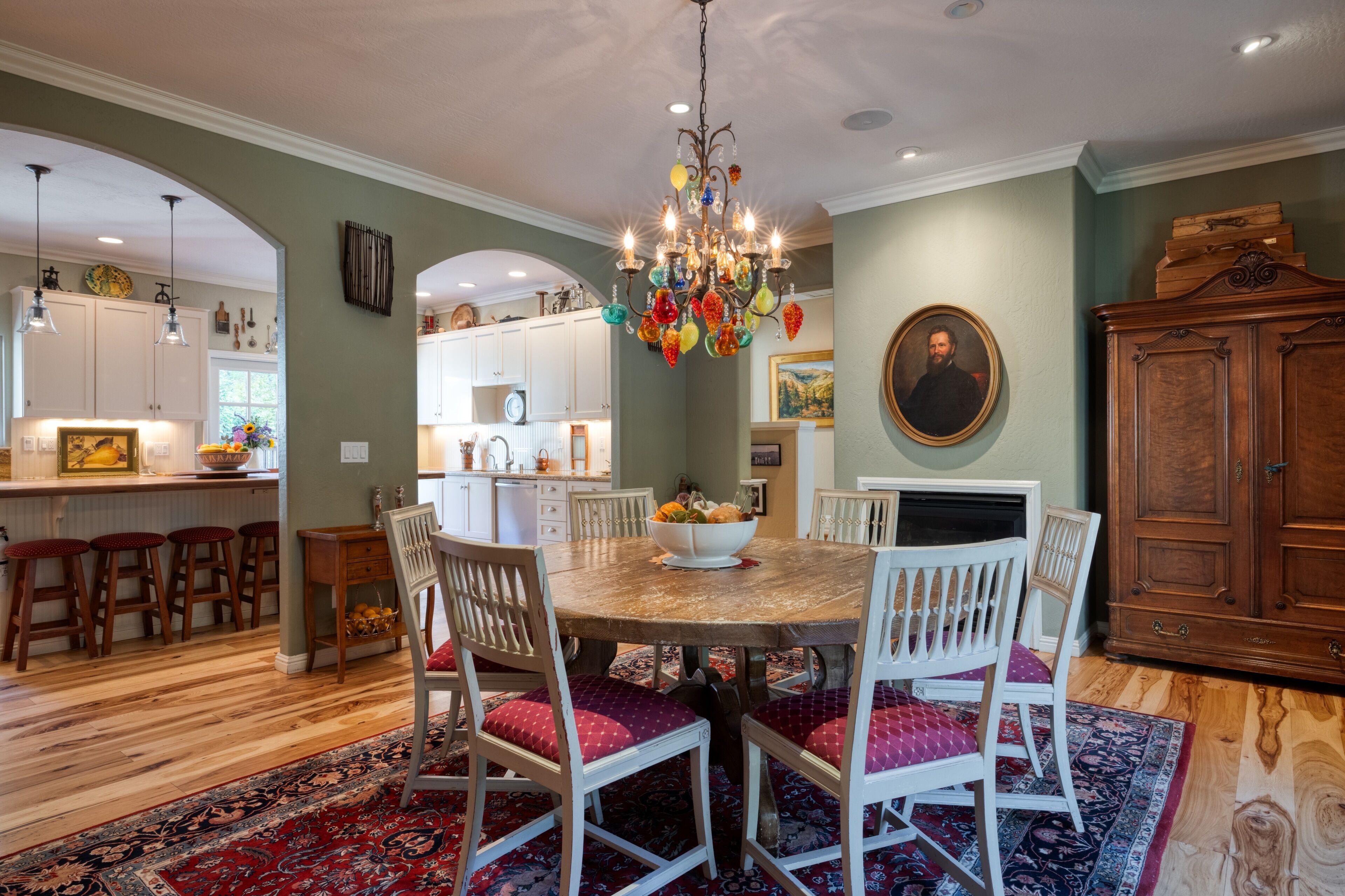 A dining area with a round table, white chairs, a chandelier, and a wooden cabinet.
