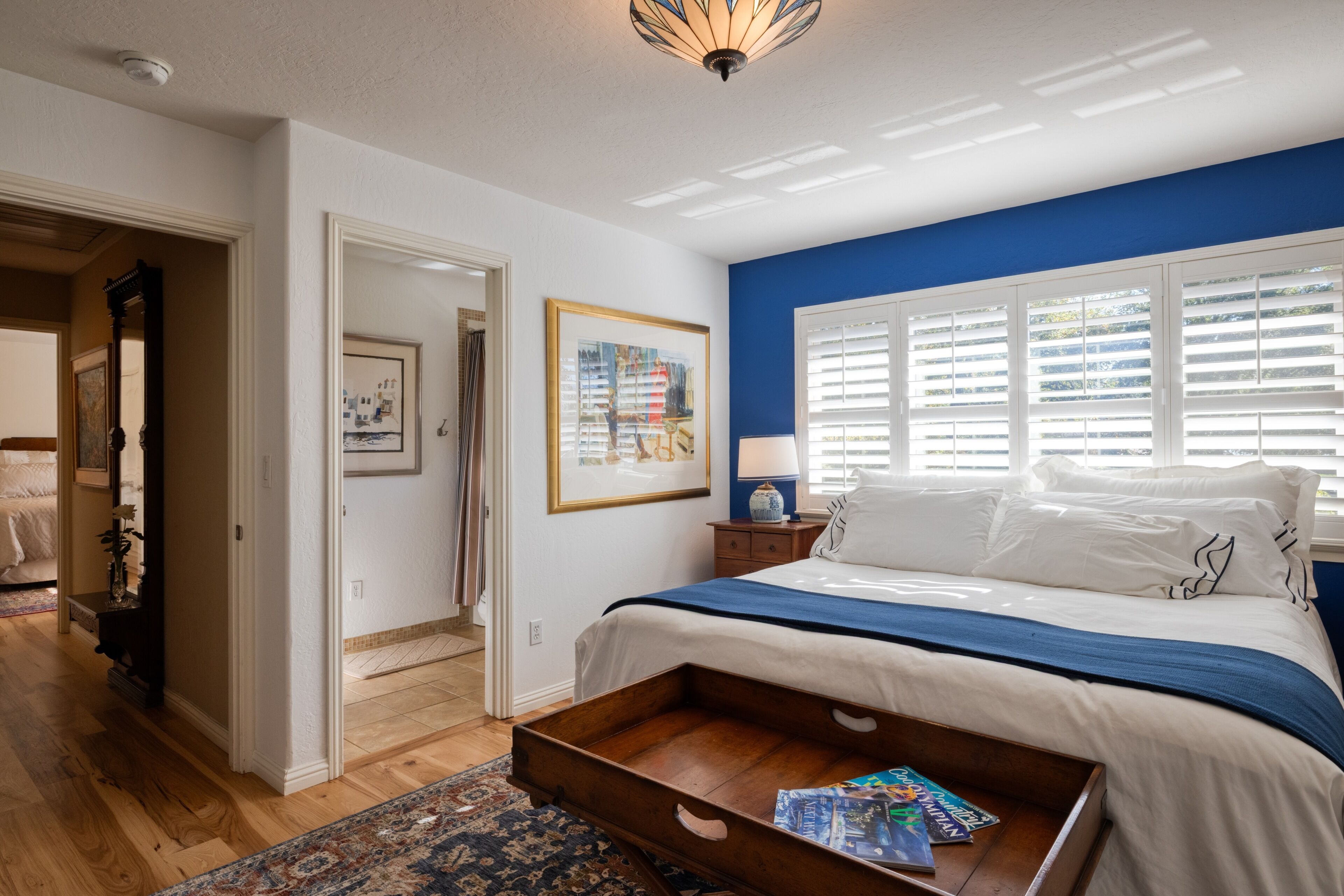 A bedroom with a bed, a wooden nightstand, a lamp, a framed picture, and a window with blinds.