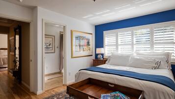 A bedroom with a bed, a wooden nightstand, a lamp, a framed picture, and a window with blinds.
