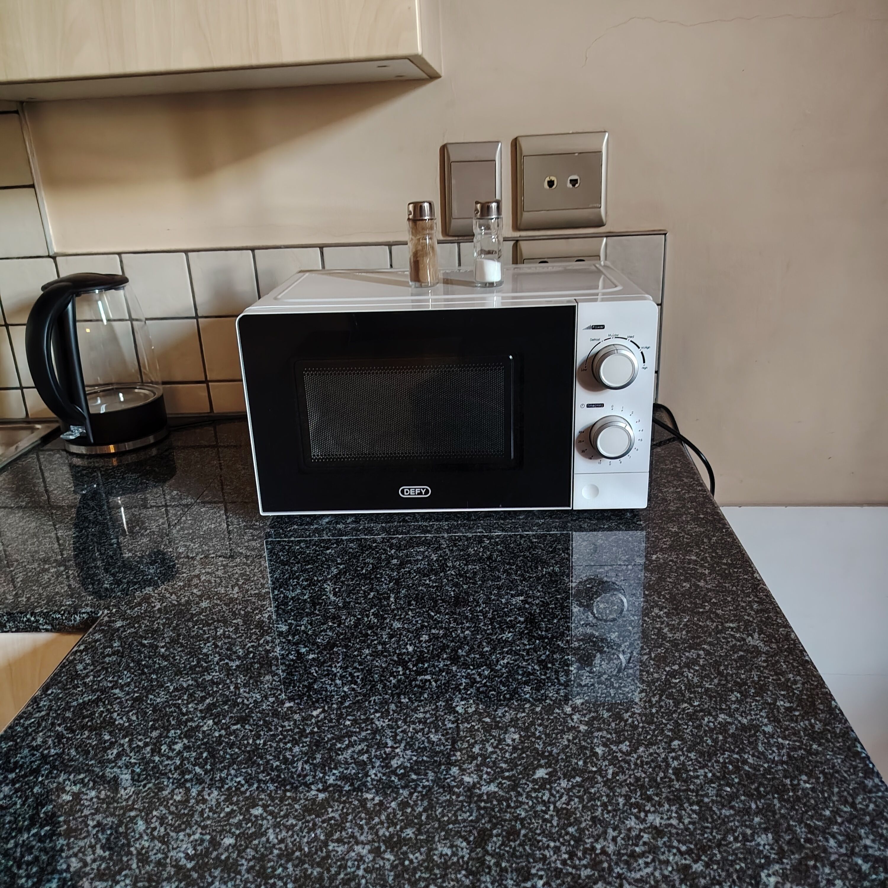 A kitchen with a black and white microwave, a kettle, and a spice rack.